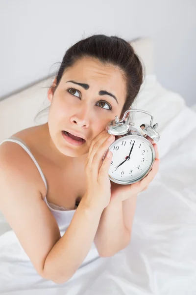 Ενοχλημένος γυναίκα που κρατά ένα ξυπνητήρι στο κρεβάτι — Φωτογραφία Αρχείου