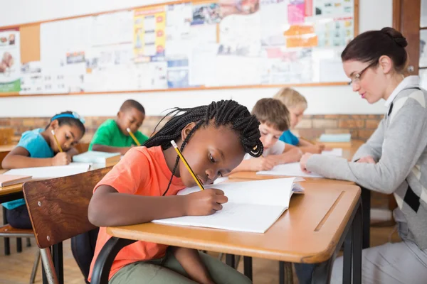 Pupils writing at desk in classroom — Stock Photo, Image