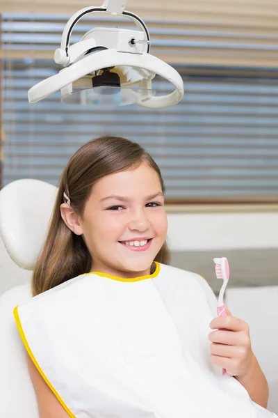 Chica sosteniendo cepillo de dientes en silla de dentistas —  Fotos de Stock