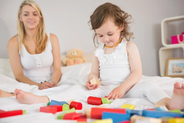 Mor och dotter leker med byggstenar på sängen — Stockfoto