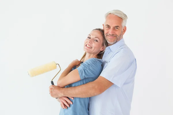 Casal feliz abraçando e segurando rolo de pintura — Fotografia de Stock