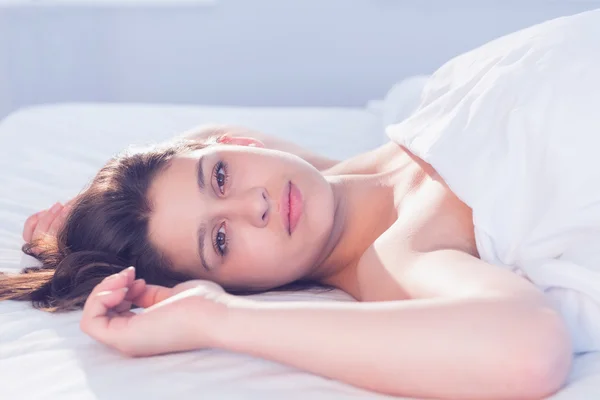 Krásná brunetka ležící na posteli se usmívá na kameru — Stock fotografie