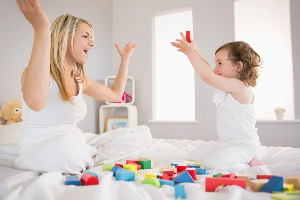 Mor och dotter leker med byggstenar på sängen — Stockfoto