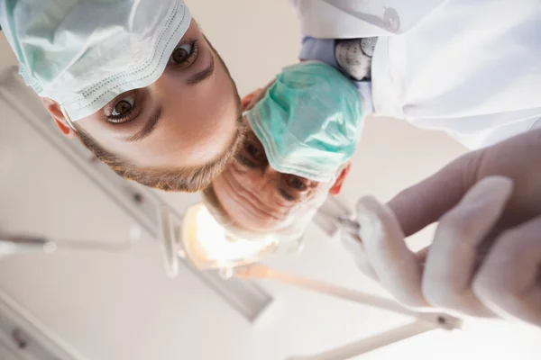 Dentista e assistente inclinados sobre o paciente — Fotografia de Stock