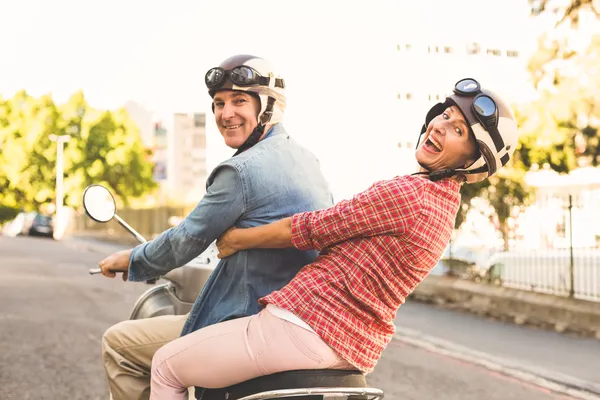 Happy mature couple riding a scooter in the city — Stock Photo, Image