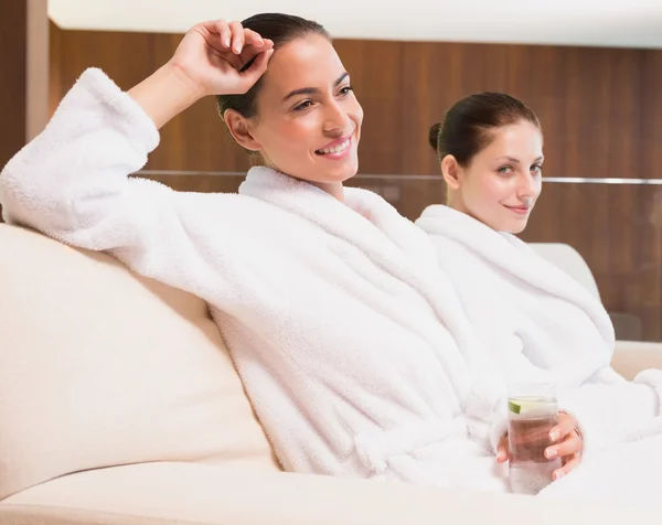 Lächelnde Frauen in Bademänteln, die Wasser trinken — Stockfoto