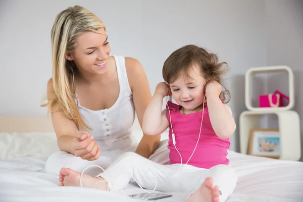 Мати дивиться на дочку з навушниками на ліжку — стокове фото