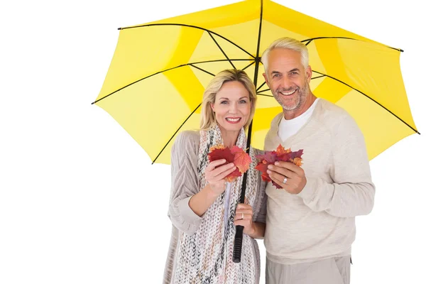 Casal sorridente mostrando folhas de outono sob guarda-chuva — Fotografia de Stock