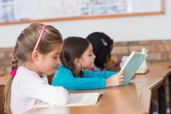 Lindos alumnos leyendo libros en sus escritorios — Foto de Stock