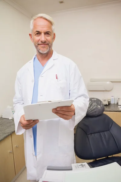 Dentista sonriendo a la cámara sujetando portapapeles — Foto de Stock