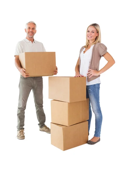 Happy couple smiling at camera with moving boxes — Stock Photo, Image
