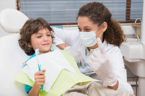 Odontólogo pediátrico mostrando al niño en silla el cepillo de dientes —  Fotos de Stock