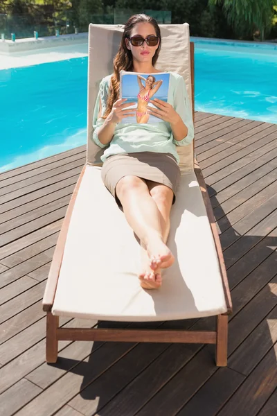 Mujer leyendo libro sobre tumbona junto a la piscina — Foto de Stock