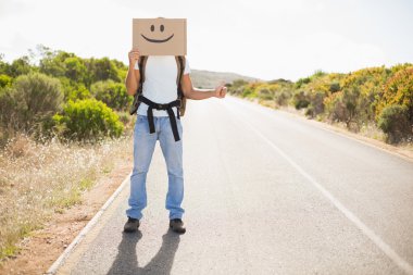 Man with smiley face hitchhiking on countryside road clipart