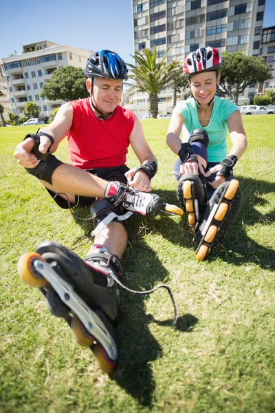 Fit mature couple tying up their roller blades on the grass — Stock Photo, Image