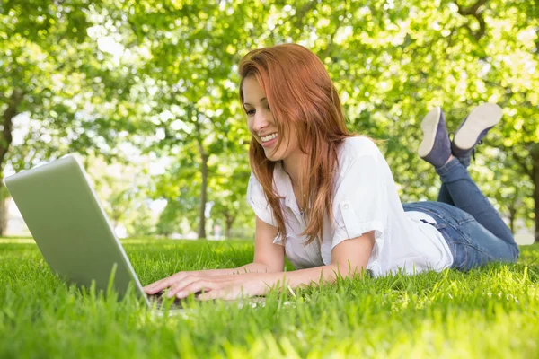 Ruiva sorridente usando laptop no parque — Fotografia de Stock