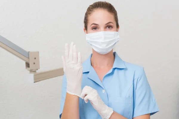 Zahnarzthelferin in Maske blickt in Kamera und zieht Handschuhe an — Stockfoto