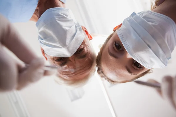 Dentista e assistente inclinados sobre o paciente — Fotografia de Stock