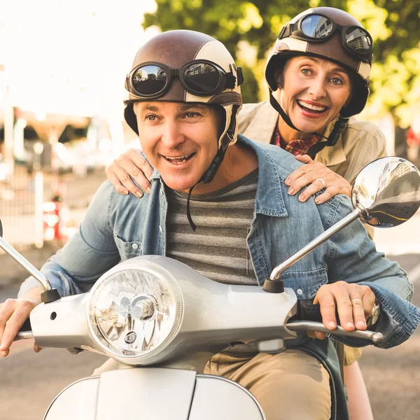 Felice coppia matura cavalcando uno scooter in città — Foto Stock