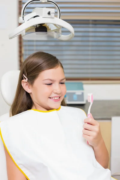 Chica sosteniendo cepillo de dientes en silla de dentistas — Foto de Stock