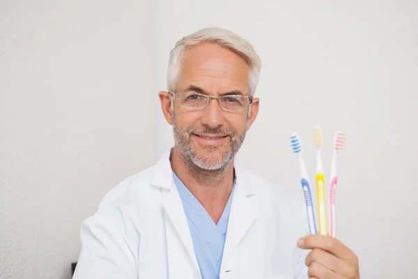 Dentist smiling at camera holding toothbrushes — Stock Photo, Image