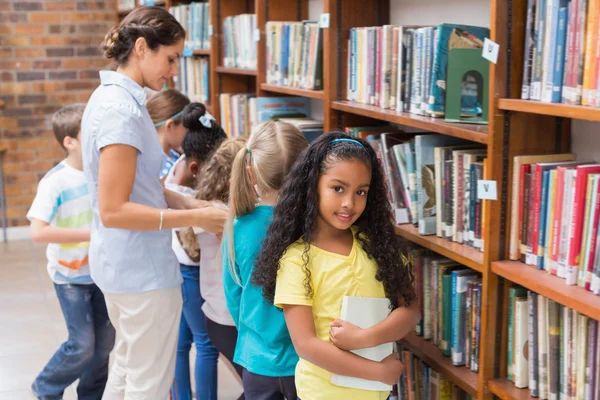 Pupils and teacher looking for books in library — Stock fotografie