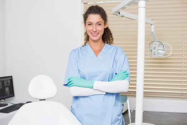 Dentista em azul esfrega sorrindo para a câmera ao lado da cadeira — Fotografia de Stock