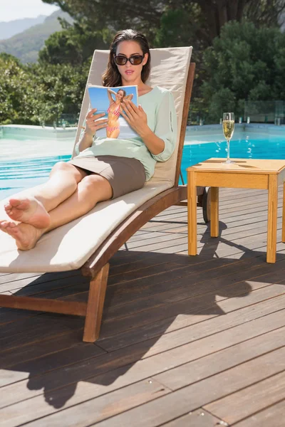 Woman reading book on sun lounger by pool — Stock Photo, Image