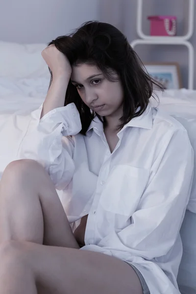 Morena triste sentada no chão ao lado de sua cama — Fotografia de Stock