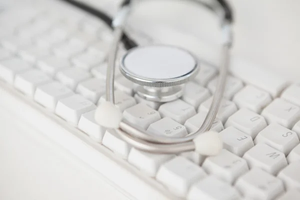 Estetoscopio tumbado sobre teclado blanco —  Fotos de Stock