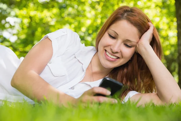 Redhead liggen op het gras verzenden van een tekst — Stockfoto