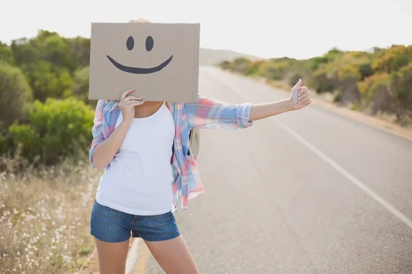 Woman with smiley face hitchhiking on countryside road — Stock Photo, Image