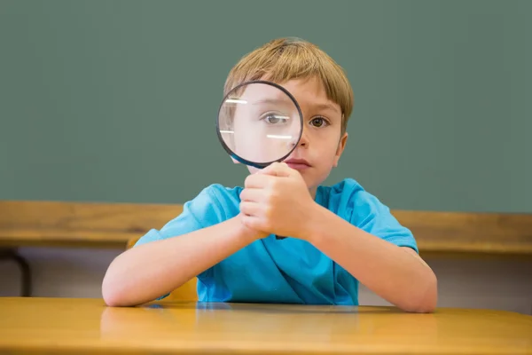 Pupil in classroom holding magnifying glass — Stock Photo, Image