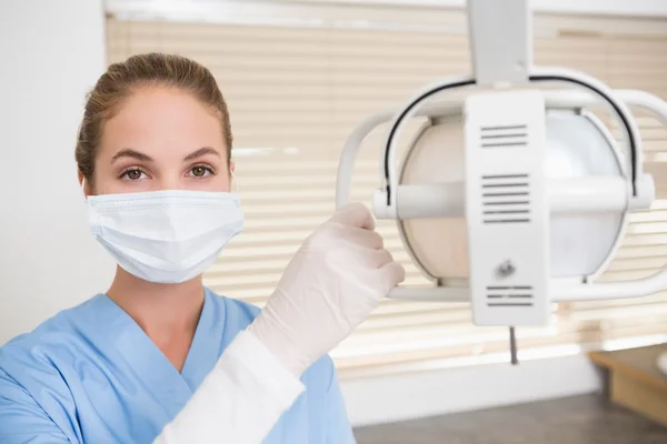 Dentista em máscara cirúrgica ajustando a luz — Fotografia de Stock