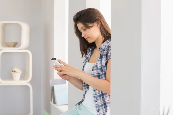 Pretty brunette sitting beside her window sending a text — Stock Photo, Image