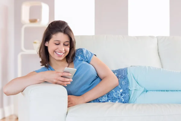 Pretty brunette sending a text on the couch — Stock Photo, Image