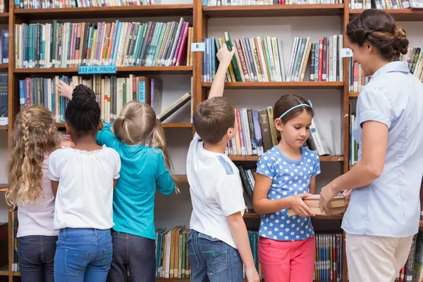 Pupils and teacher looking for books in library — Stock fotografie