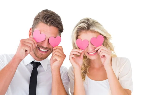 Atractiva pareja joven sosteniendo corazones rosados sobre los ojos — Foto de Stock
