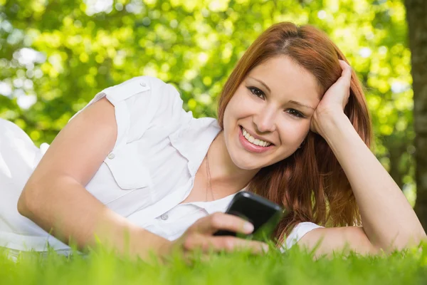 Redhead liggen op het gras verzenden van een tekst — Stockfoto