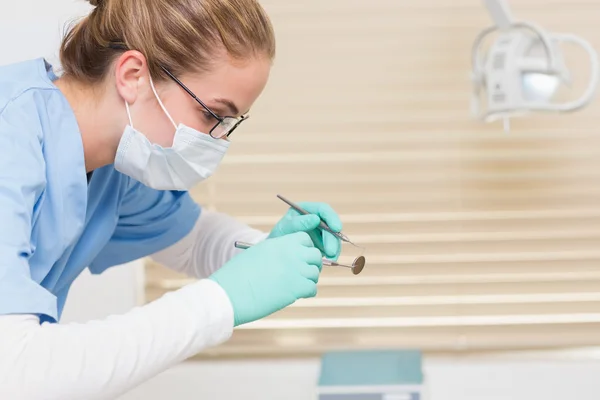 Dentista en matorrales azules sosteniendo herramientas dentales —  Fotos de Stock