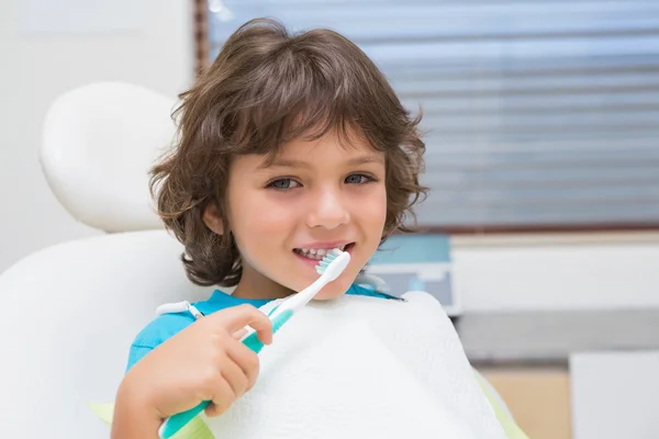 Ragazzino in sedia dentisti utilizzando spazzolino da denti — Foto Stock
