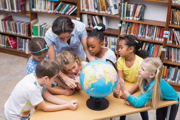 Alunos e professor olhando para o globo na biblioteca — Fotografia de Stock