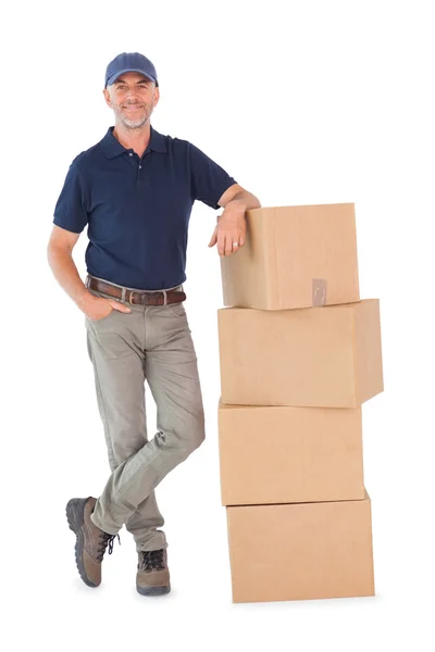 Happy delivery man leaning on pile of cardboard boxes — Stock Photo, Image