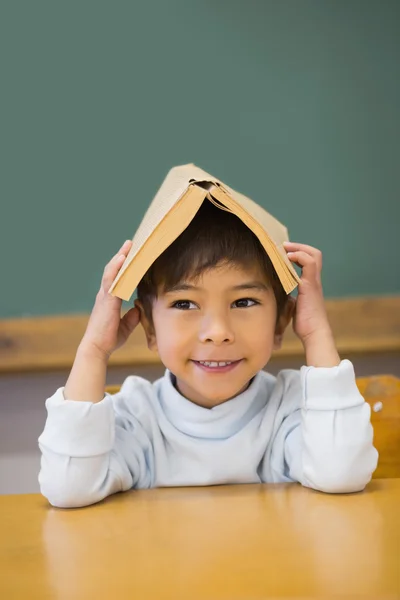 Pupil holding book on his head at desk — Stock Photo, Image