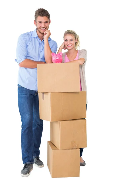 Attractive young couple leaning on boxes with piggy bank — Stock Photo, Image