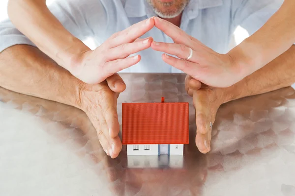 Couple sheltering miniature house with hands — Stock Photo, Image