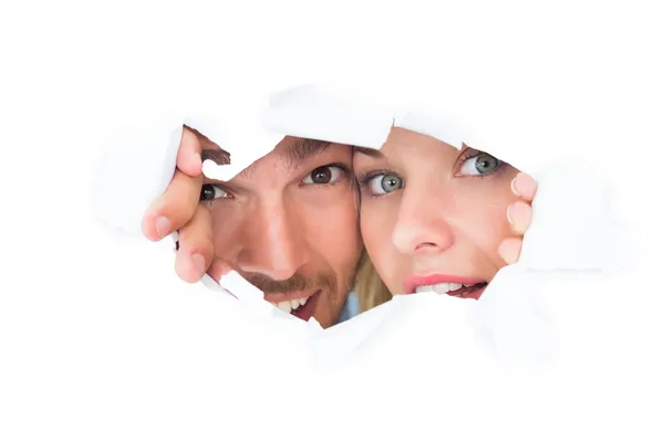 Giovane coppia sbirciando attraverso carta strappata — Foto Stock