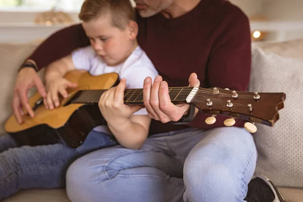 코카서스 아버지의 섹션은 아들에게 소파에 기타를 연주하는 가르친다 — 스톡 사진