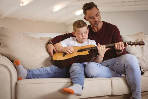 Padre Caucásico Enseñando Hijo Tocar Guitarra Sentado Sofá Casa Concepto —  Fotos de Stock