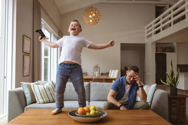 家庭で父親とビデオゲームをしながらテーブルの上に立って祝う白人の少年 ゲームやエンターテイメントのコンセプト — ストック写真